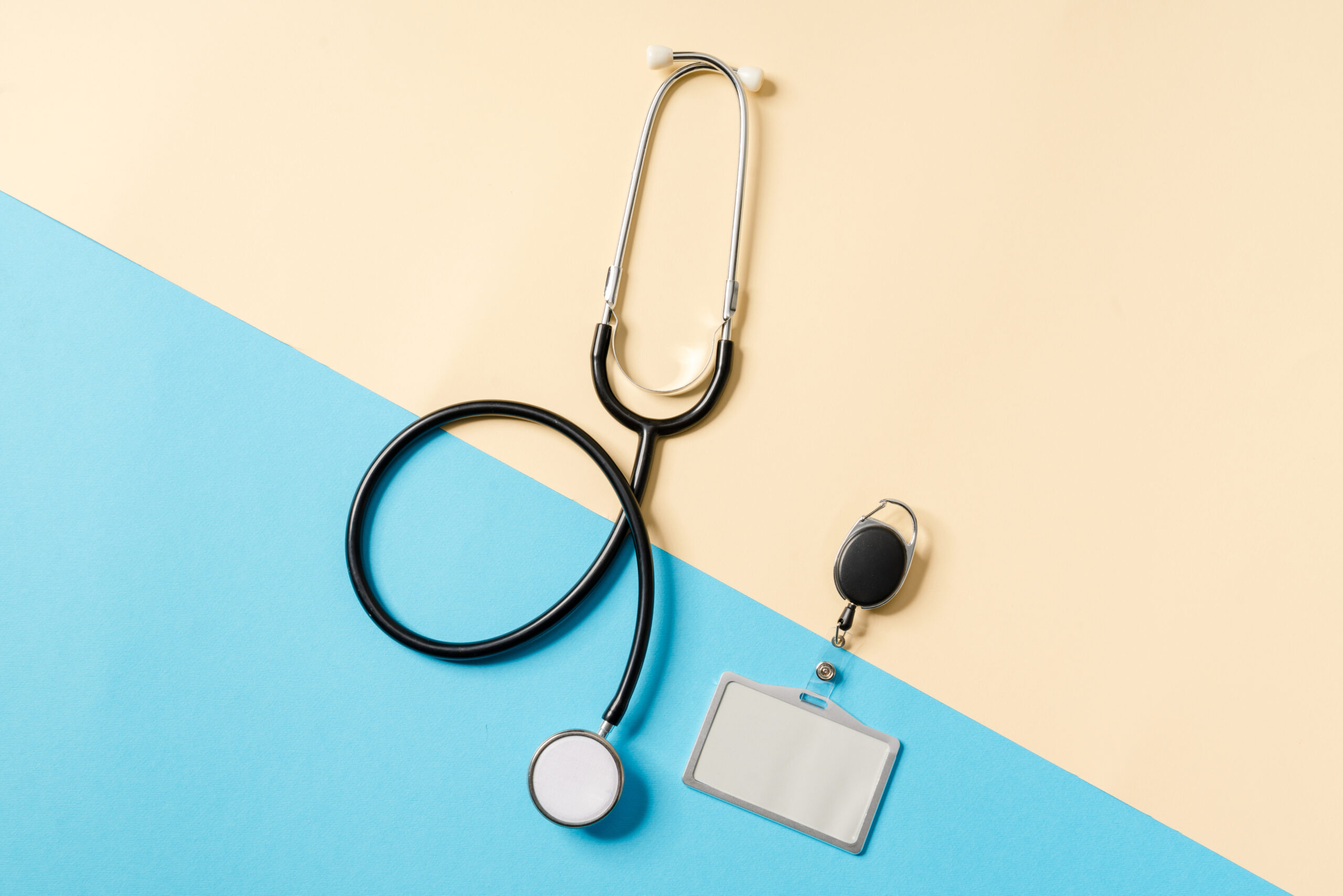 Overhead view of a badge with a stethoscope lying on a beige and blue background in the studio