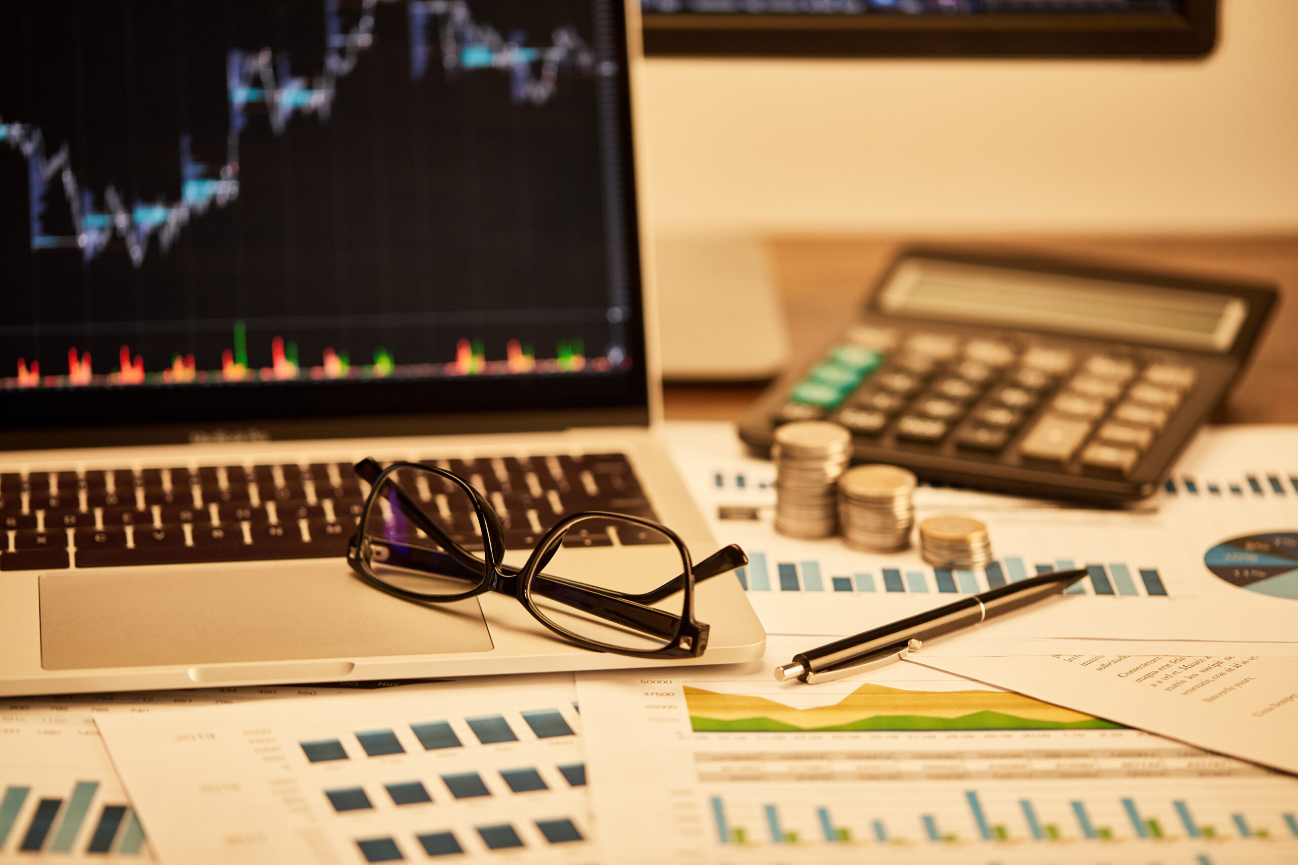 selective focus of laptop, coins, papers, glasses, pen and calculator on table