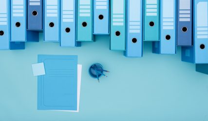 Archive binders in a row and monochrome desktop with files and stationery, top view