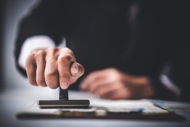 Close-up Of A Person's Hand Stamping With Approved Stamp On Text Approved Document At Desk,  Contract Form Paper