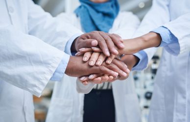 Shot of a group of unrecognisable scientists joining hands in solidarity in a laboratory.